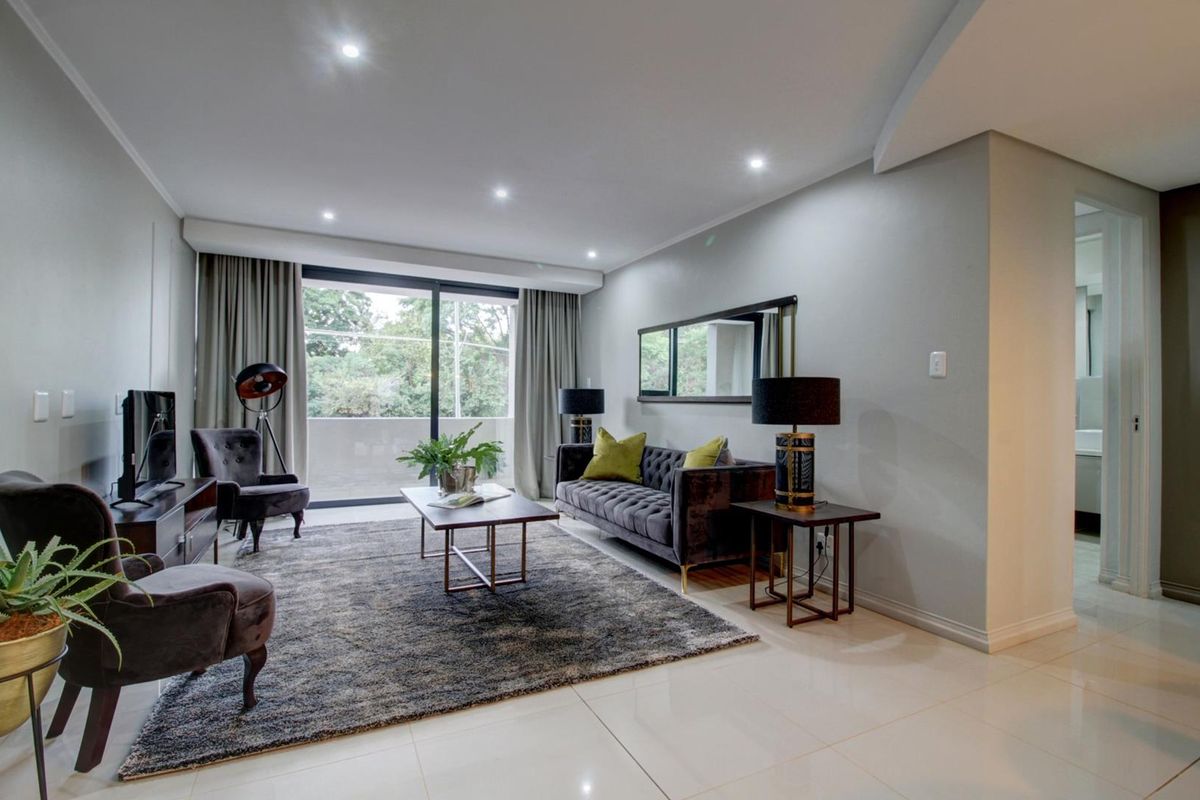 A well-maintained living room featuring modern recessed downlights, sleek tiled flooring, and a large sliding glass door providing access to the balcony.