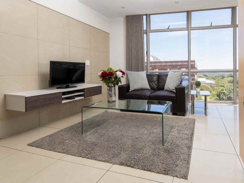 A bright and modern living room featuring large floor-to-ceiling windows, neutral tiled flooring, and sleek wall-mounted cabinetry with a contemporary aesthetic.