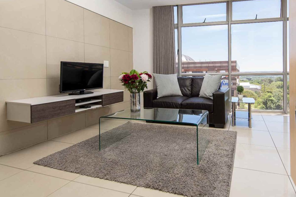 A bright and modern living room featuring large floor-to-ceiling windows, neutral tiled flooring, and sleek wall-mounted cabinetry with a contemporary aesthetic.