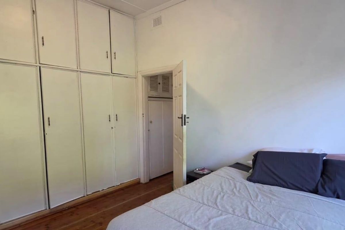 Bedroom featuring extensive floor-to-ceiling built-in cupboards, timber flooring, and access to an adjoining space.