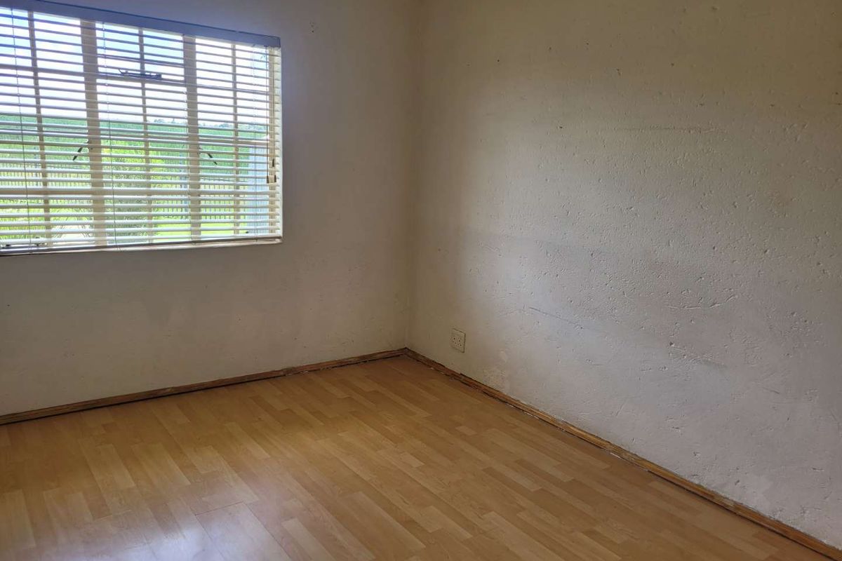 An empty bedroom featuring light wood-look laminate flooring, a window with fitted blinds, and plain walls requiring cosmetic attention.