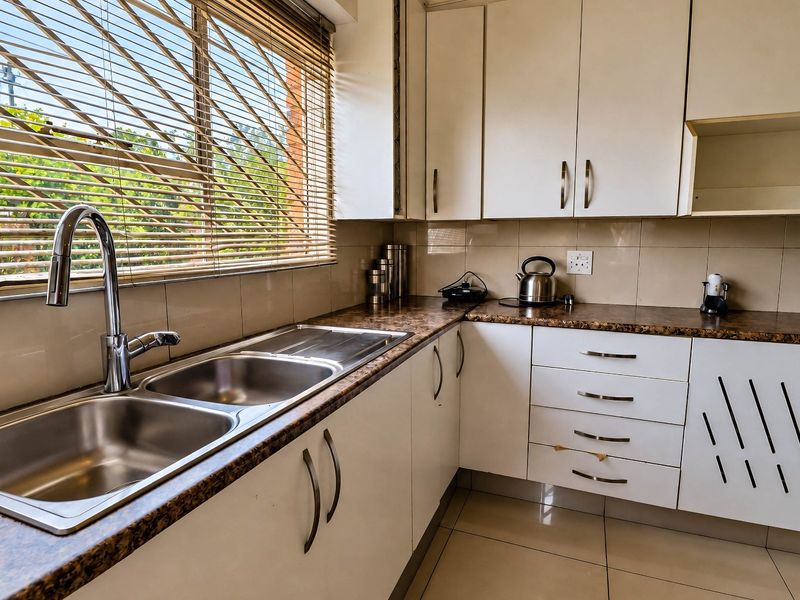 A functional kitchen featuring white cabinetry, laminate countertops, a double stainless steel sink, and tiled flooring with natural light from the window.