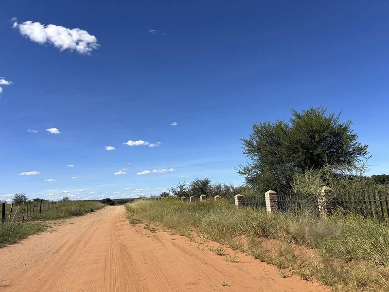 A view of the dirt road approach leading to the property, featuring perimeter fencing with brick pillars along the boundary.
