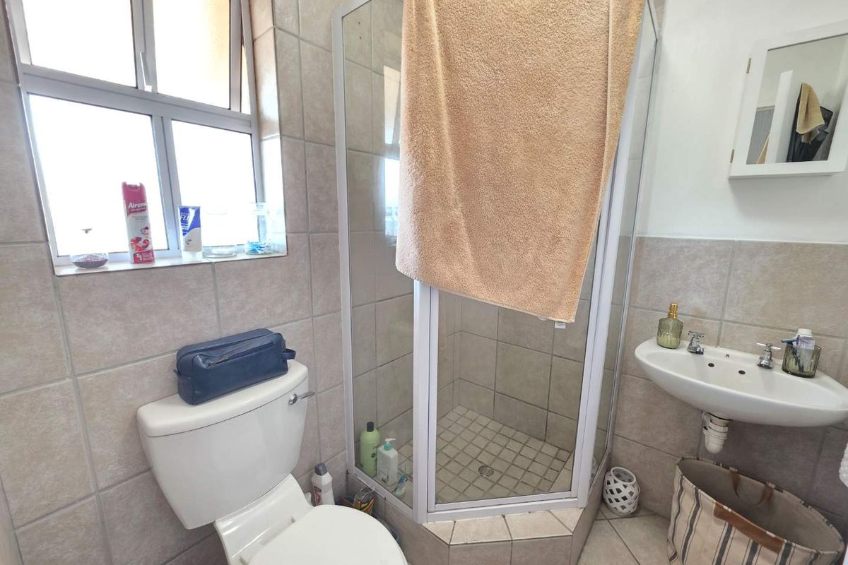 A functional bathroom featuring a corner shower enclosure, pedestal washbasin, toilet, and neutral ceramic tiling throughout.