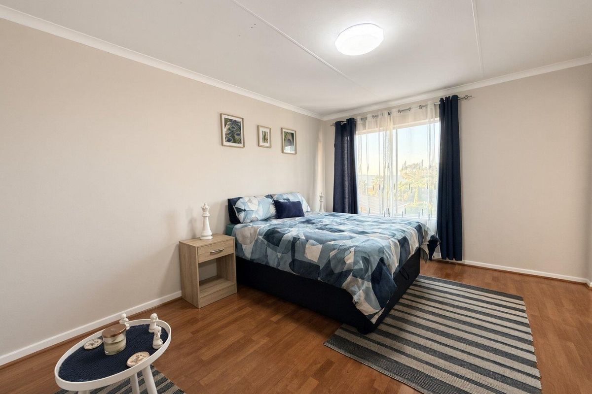 A well-maintained bedroom featuring laminate flooring, neutral wall tones, and a large window with curtain fixtures, providing a bright and comfortable living space.