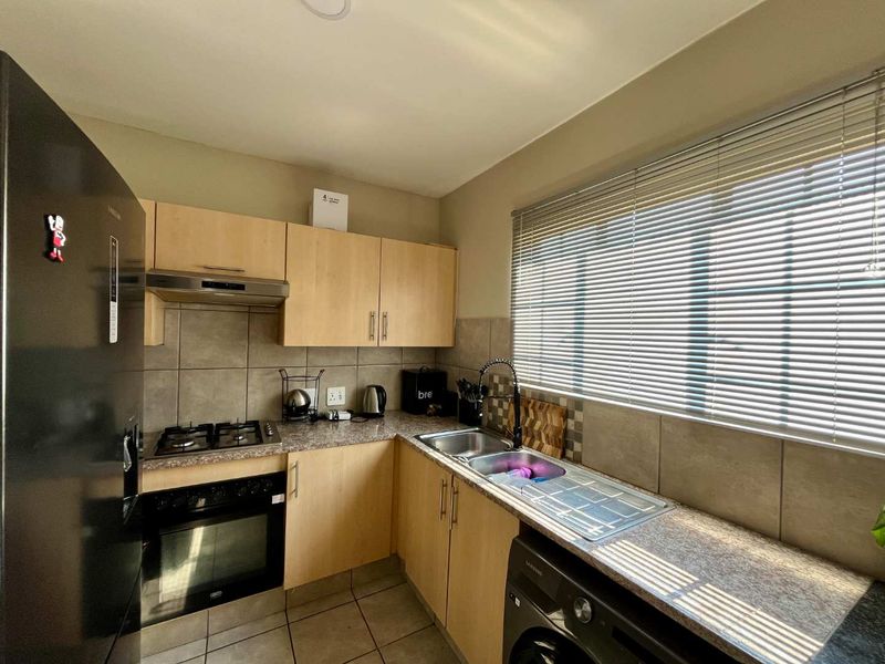 A functional kitchen featuring light wood cabinetry, granite countertops, a gas hob, built-in oven, and a double sink with tiled backsplash.