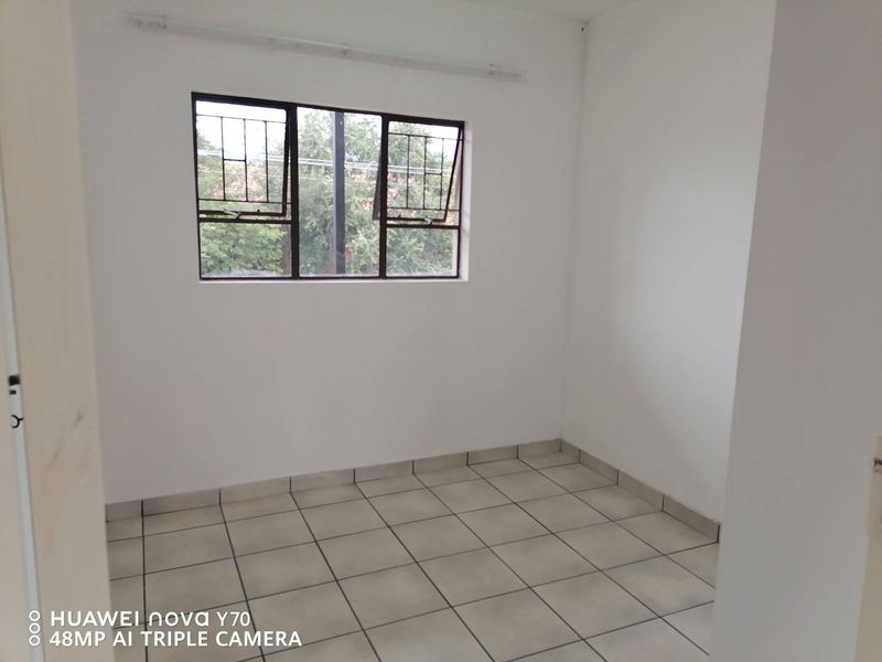 A clean, empty bedroom featuring neutral tiled flooring and a window fitted with security bars, offering a blank canvas for personalization.