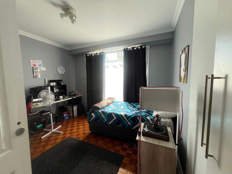 A bedroom featuring classic parquet flooring, crown molding, and a window allowing natural light, providing a functional space for rest or study.