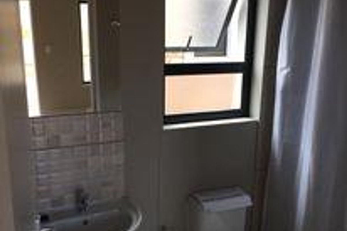 A functional bathroom featuring a wall-mounted basin, a standard toilet, and a shower area with a curtain, illuminated by a window.