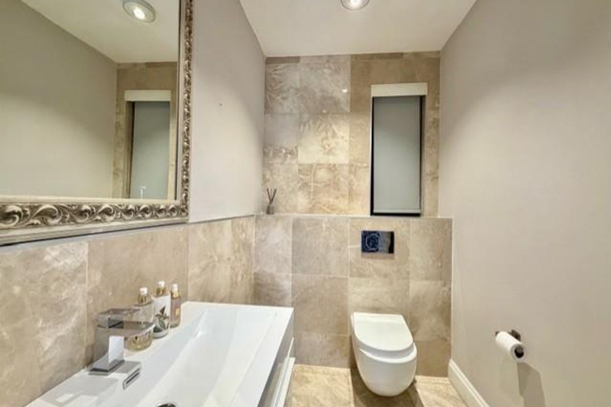 Modern guest bathroom featuring stone wall tiling, a wall-mounted toilet with concealed cistern, and a sleek vanity basin with a decorative mirror.