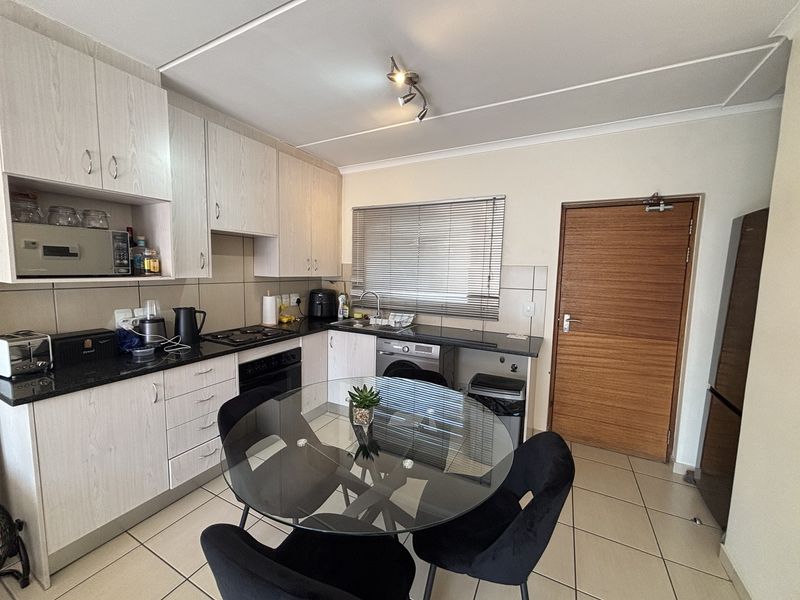 Functional kitchen featuring light wood-finish cabinetry, granite countertops, built-in oven and hob, and tiled flooring with direct access to an adjacent room.