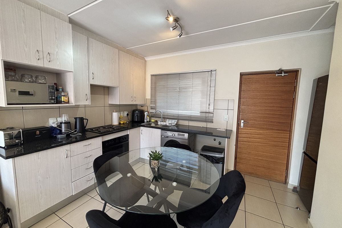 Functional kitchen featuring light wood-finish cabinetry, granite countertops, built-in oven and hob, and tiled flooring with direct access to an adjacent room.