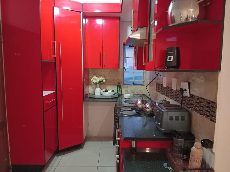 A compact kitchen featuring vibrant red high-gloss cabinetry, dark stone countertops, a stainless steel sink, and a tiled backsplash.