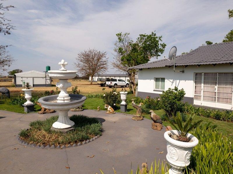 A rear garden area featuring a concrete patio, a central fountain, and a view of the main dwelling with a tiled roof.