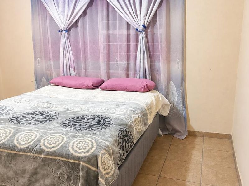 A simple bedroom featuring tiled flooring and a curtain rod, providing a functional space with neutral wall finishes.