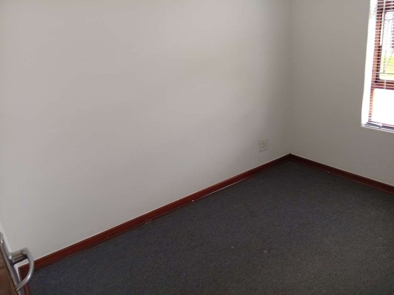 An empty bedroom featuring neutral walls, carpeted flooring, and a window with fitted venetian blinds.