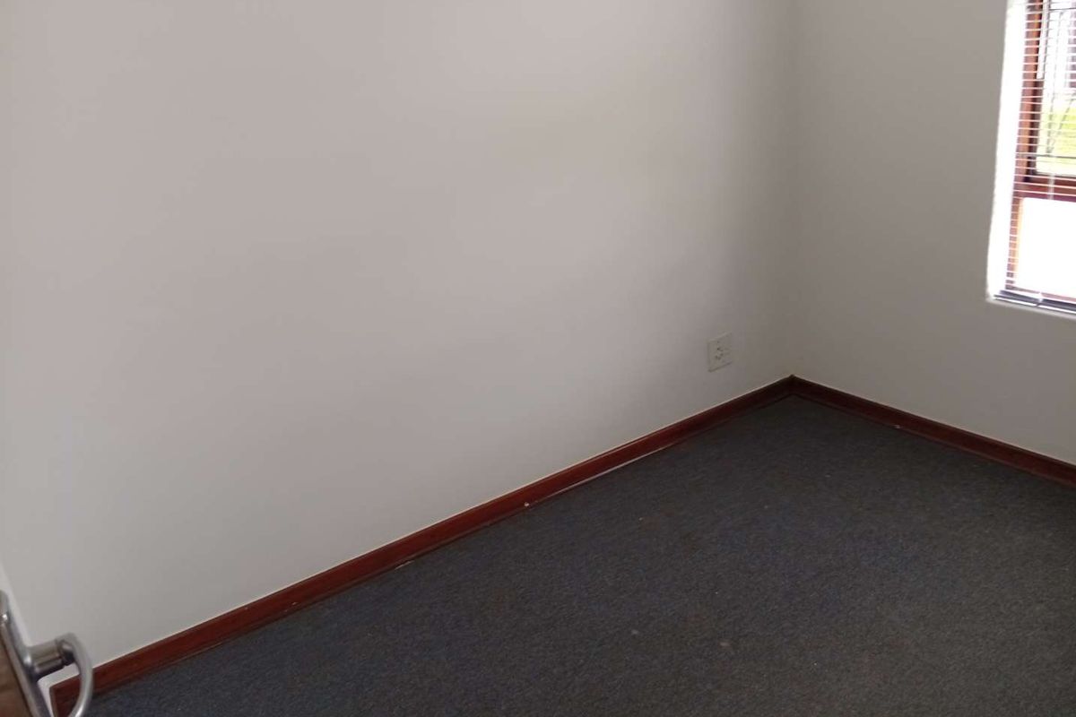 An empty bedroom featuring neutral walls, carpeted flooring, and a window with fitted venetian blinds.
