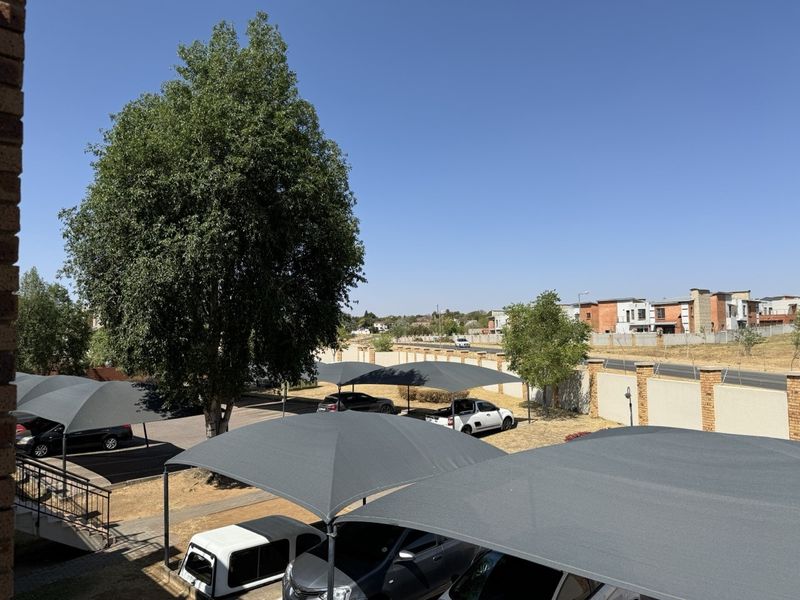 View of the apartment complex parking area featuring multiple shade cloth carports and a secure perimeter wall.