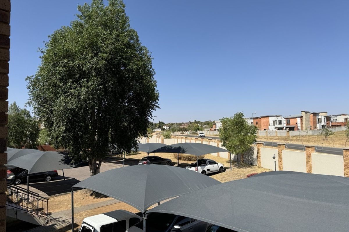 View of the apartment complex parking area featuring multiple shade cloth carports and a secure perimeter wall.