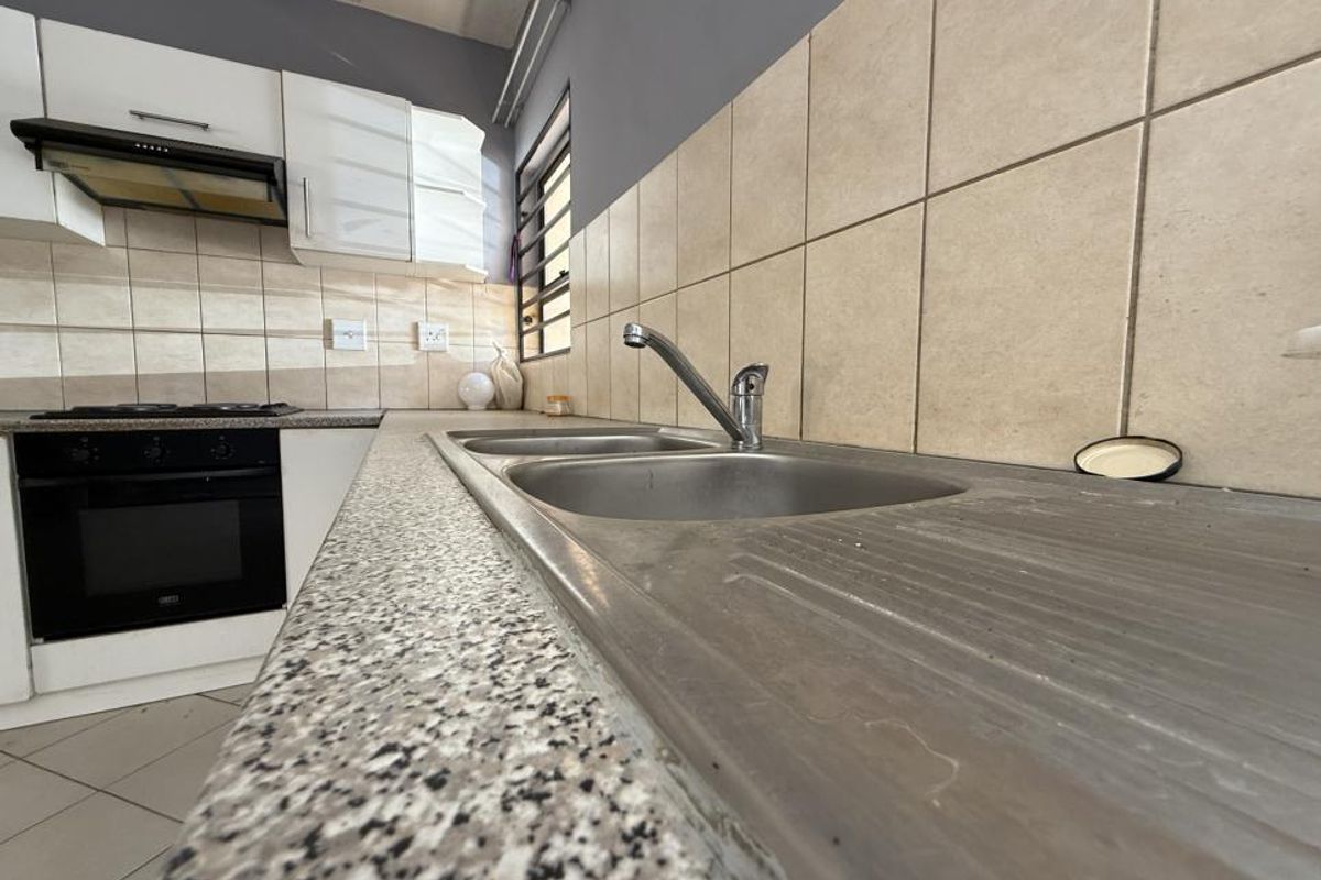 A functional kitchen featuring a stainless steel double sink, granite-look laminate countertops, built-in oven, gas hob, and overhead extractor fan.