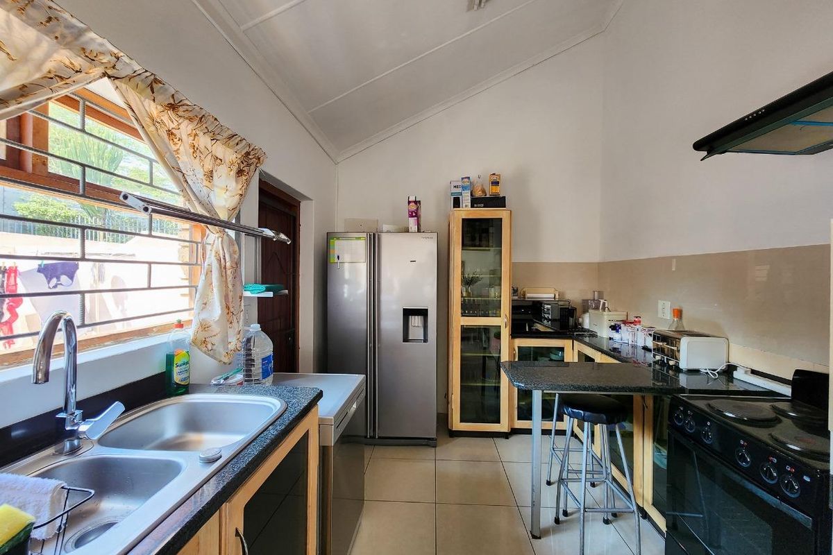 A functional kitchen featuring granite countertops, a double stainless steel sink, built-in cabinetry, and a vaulted ceiling with exposed beams.