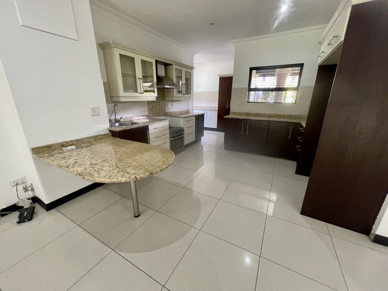 Spacious kitchen featuring granite countertops, ample built-in cabinetry, a breakfast bar, and tiled flooring in a clean, well-maintained layout.