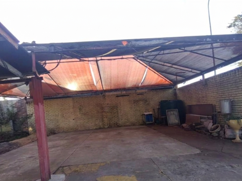 An open-sided garage or carport area featuring a concrete floor, brick walls, and a metal frame structure with damaged shade cloth roofing.