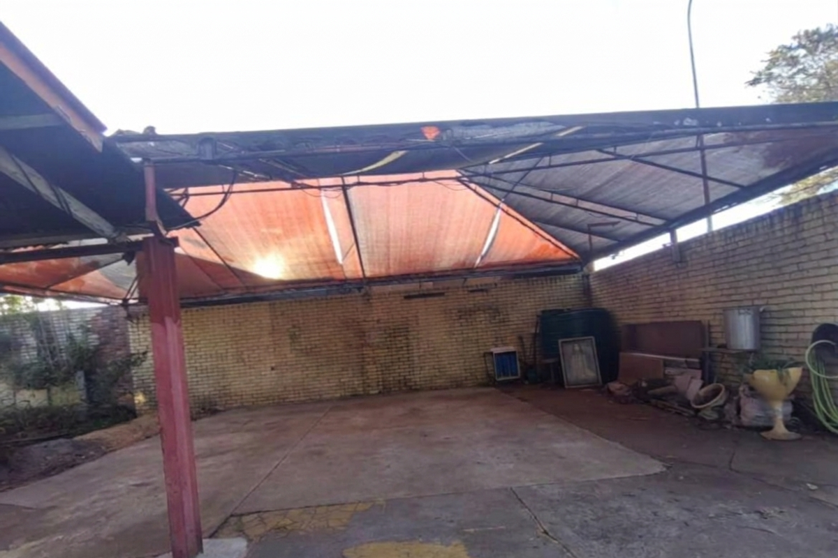 An open-sided garage or carport area featuring a concrete floor, brick walls, and a metal frame structure with damaged shade cloth roofing.