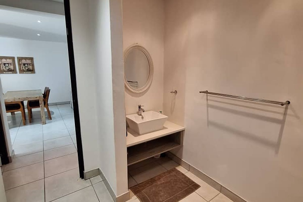 A functional bathroom vanity area featuring a modern vessel sink, wall-mounted mirror, and stainless steel towel rail, finished with neutral floor tiling.