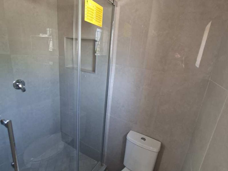 Modern bathroom featuring a glass-enclosed shower with a rain shower head, built-in niche, and a standard toilet with tiled finishes.