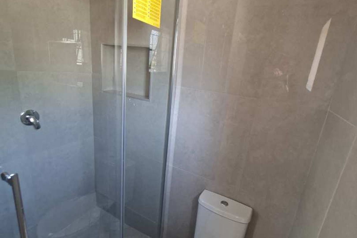 Modern bathroom featuring a glass-enclosed shower with a rain shower head, built-in niche, and a standard toilet with tiled finishes.