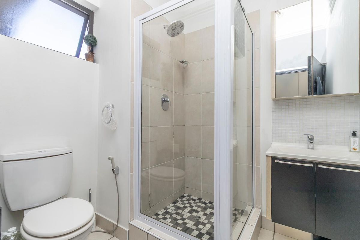 A functional bathroom featuring a glass-enclosed shower, vanity unit with integrated basin, mirror cabinet, and toilet.