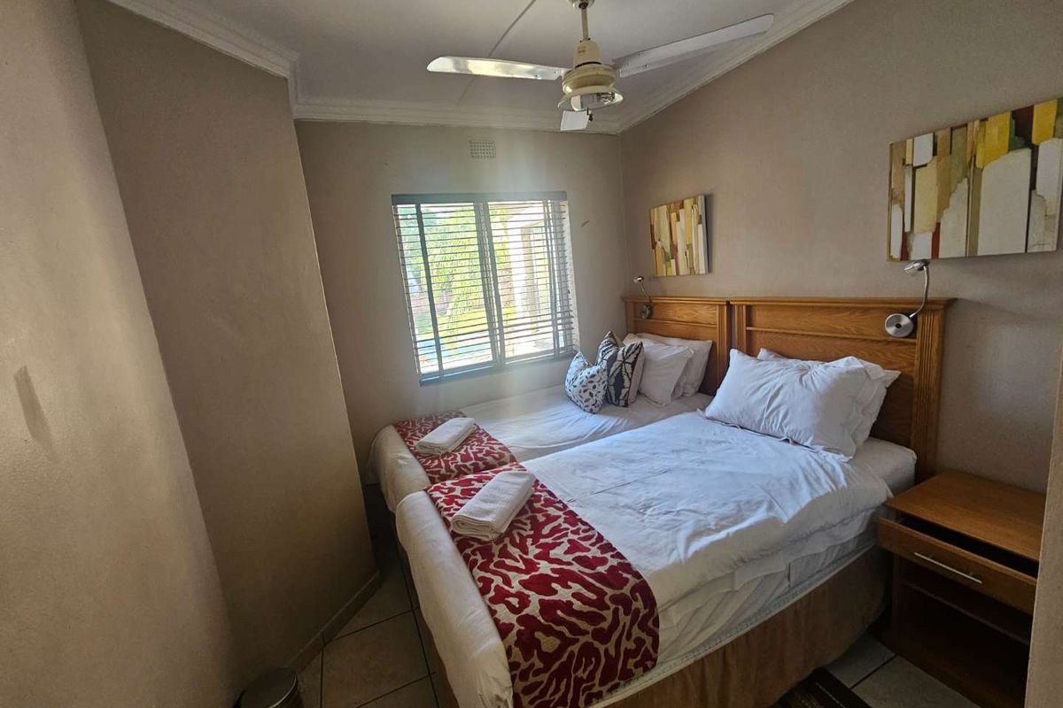 A compact bedroom featuring tiled flooring, a ceiling fan, and a window with fitted blinds, providing a functional sleeping space.