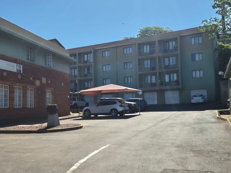 Exterior view of a multi-story apartment complex featuring an asphalt parking area, covered carports, and residential balconies.