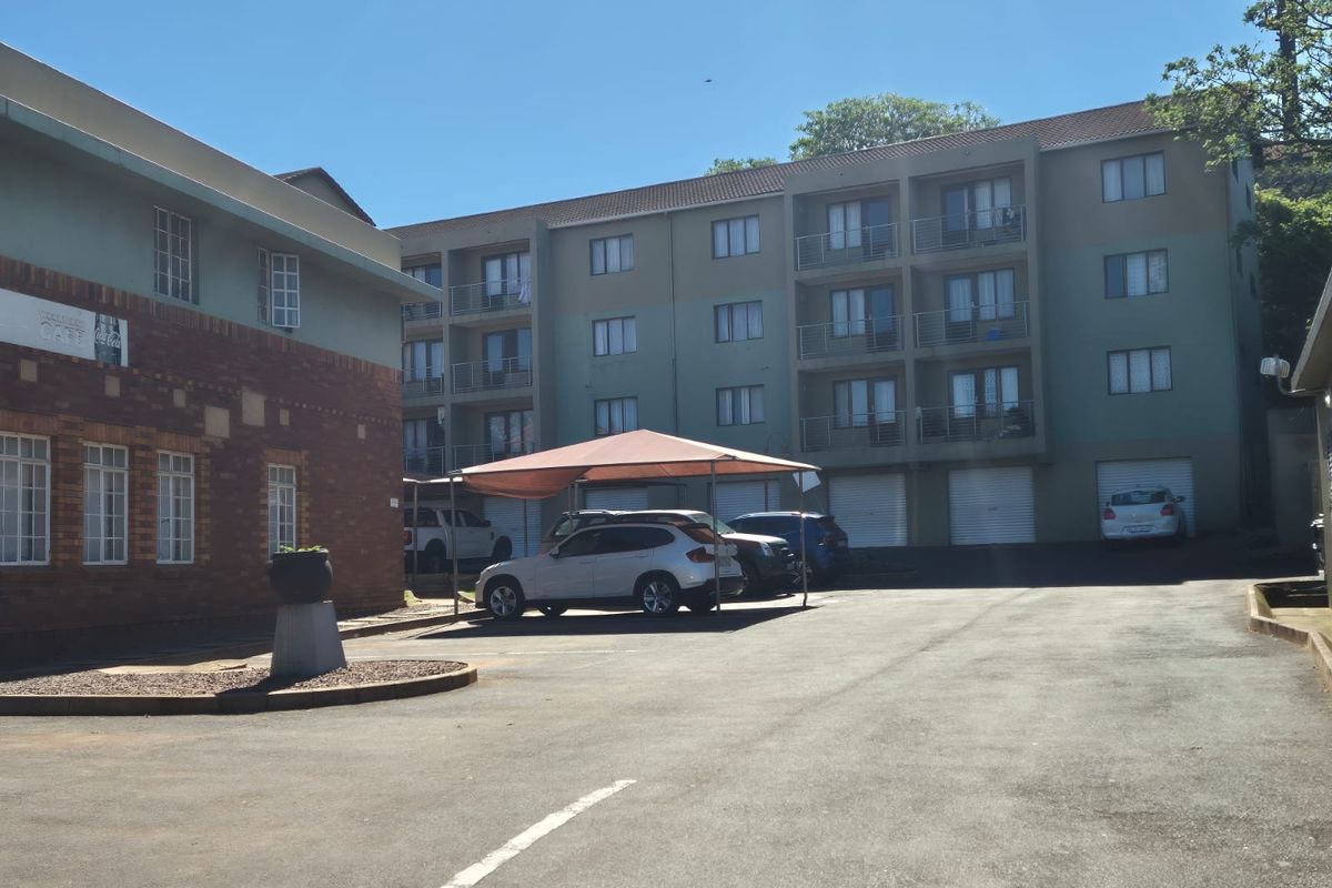 Exterior view of a multi-story apartment complex featuring an asphalt parking area, covered carports, and residential balconies.