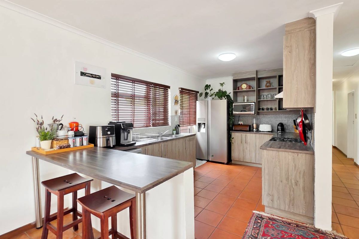 A functional kitchen featuring wood-look cabinetry, laminate countertops, a gas hob, and a breakfast bar, complemented by tiled flooring and natural light.