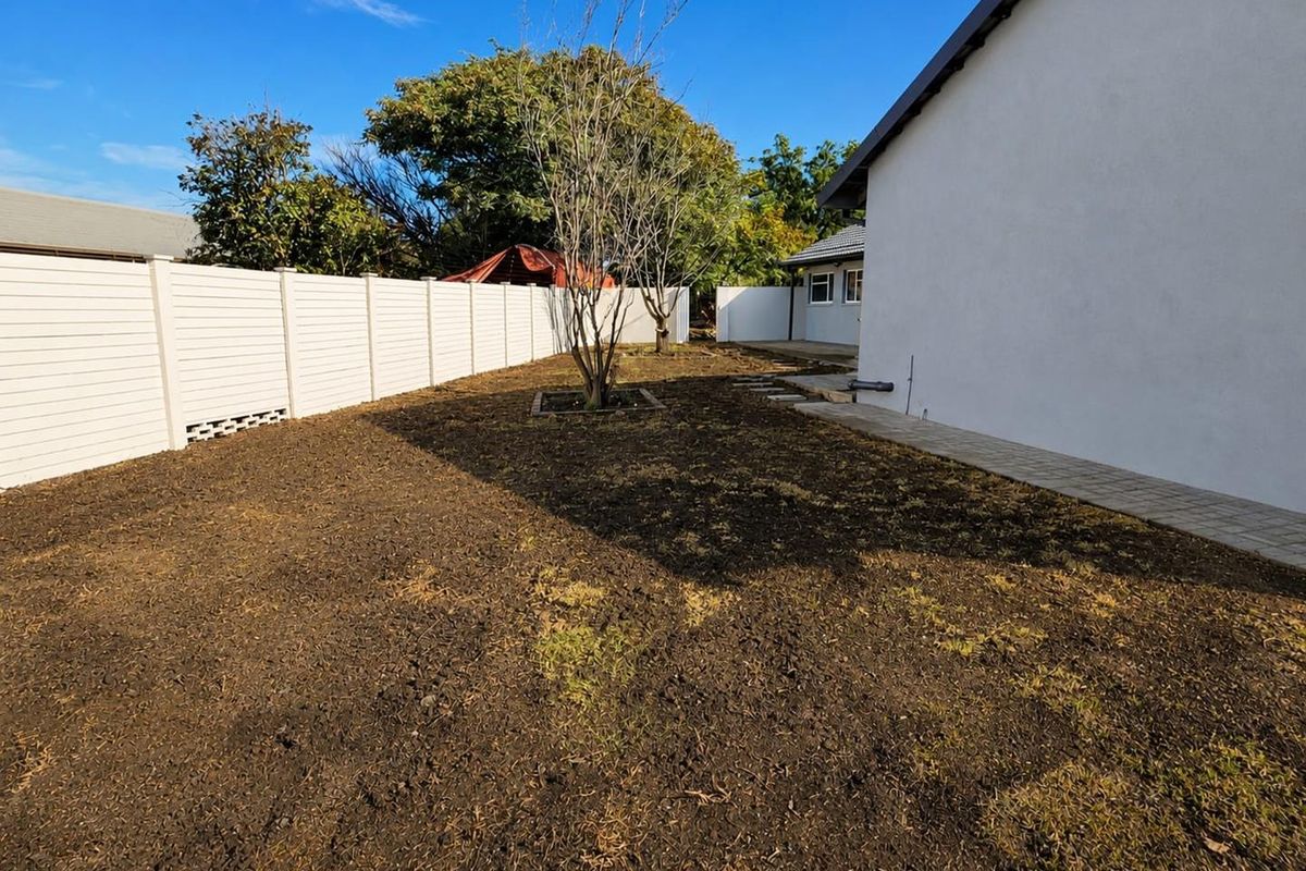 A rear garden area featuring a paved walkway along the house exterior and perimeter fencing, currently awaiting landscaping or lawn establishment.