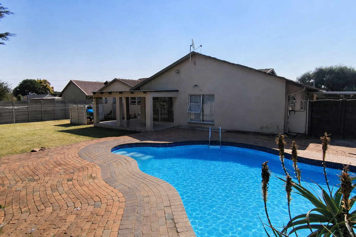 Rear exterior view featuring a swimming pool, brick paved patio area, covered veranda, and a spacious garden with boundary walling.