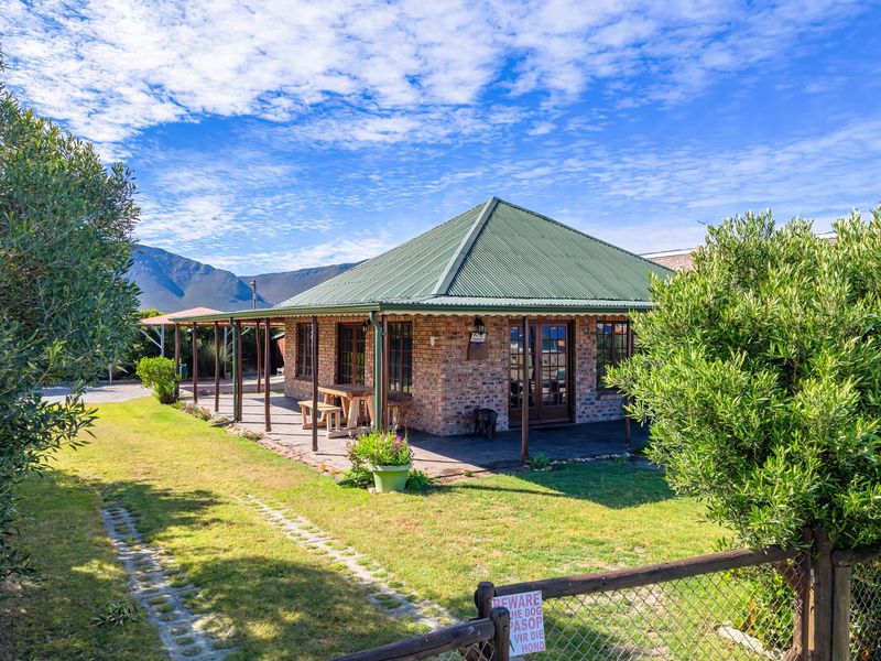 A charming face brick house featuring a wrap-around covered patio, green corrugated metal roof, and a well-maintained garden with mountain views.