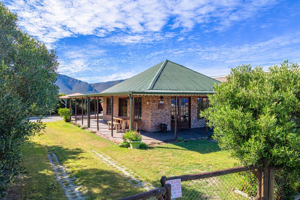 A charming face brick house featuring a wrap-around covered patio, green corrugated metal roof, and a well-maintained garden with mountain views.