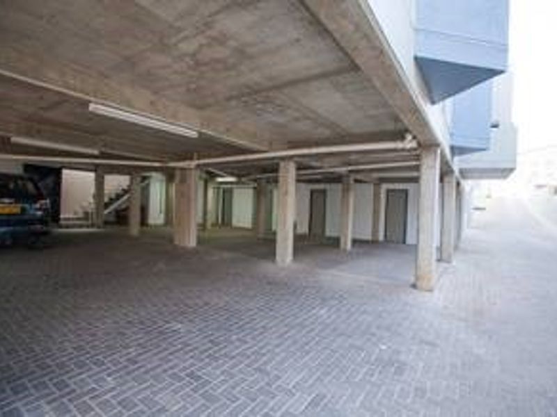A covered parking area featuring a concrete ceiling, support columns, and paved flooring, providing sheltered space for vehicles.