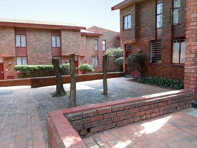 A paved rear courtyard area featuring face brick townhouse architecture, low brick retaining walls, and established landscaping.