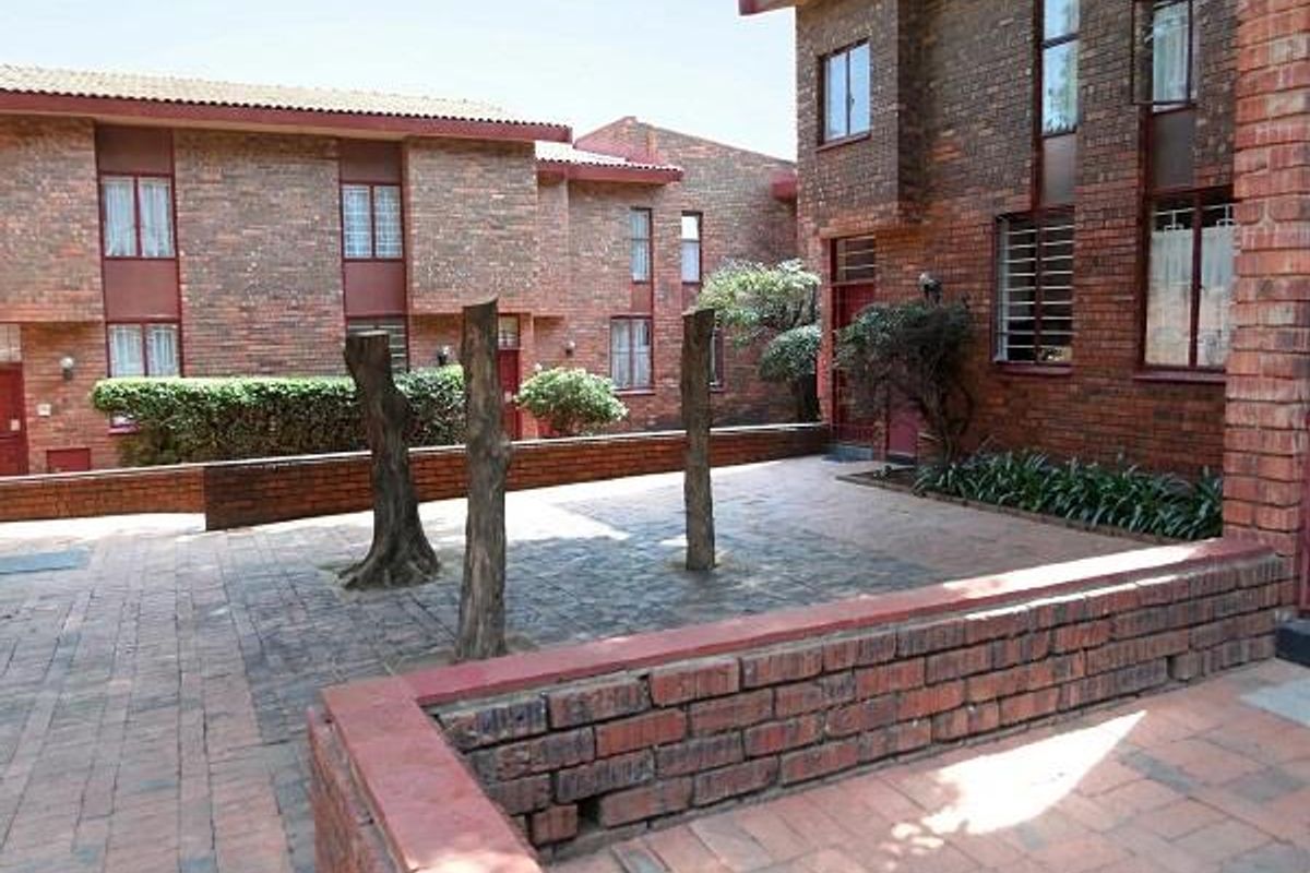 A paved rear courtyard area featuring face brick townhouse architecture, low brick retaining walls, and established landscaping.