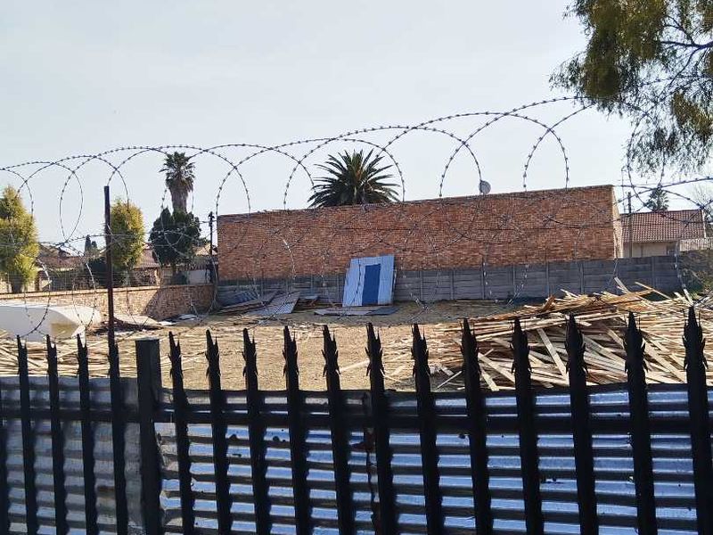 Vacant residential land enclosed by a brick boundary wall, precast concrete wall, and metal palisade fencing with security razor wire.
