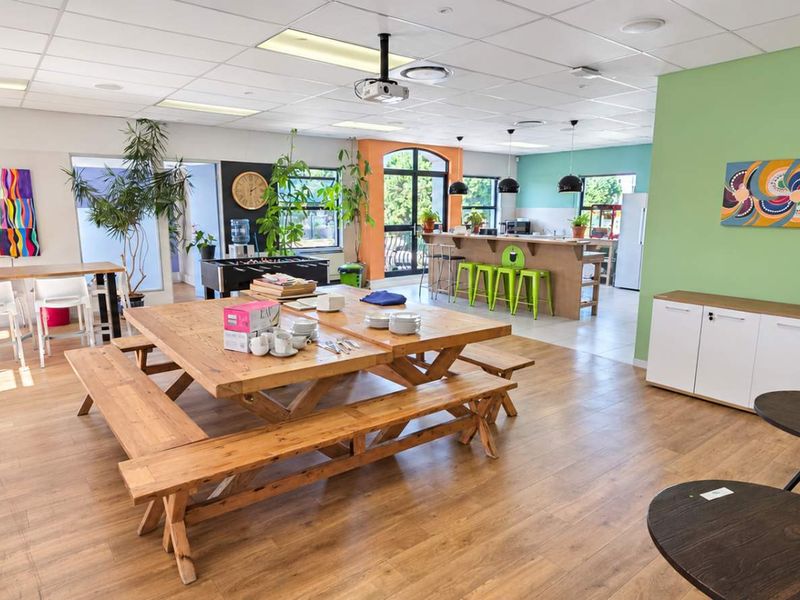 Spacious open-plan office breakout area featuring a kitchen counter, wood-look laminate flooring, and a suspended ceiling with integrated lighting.