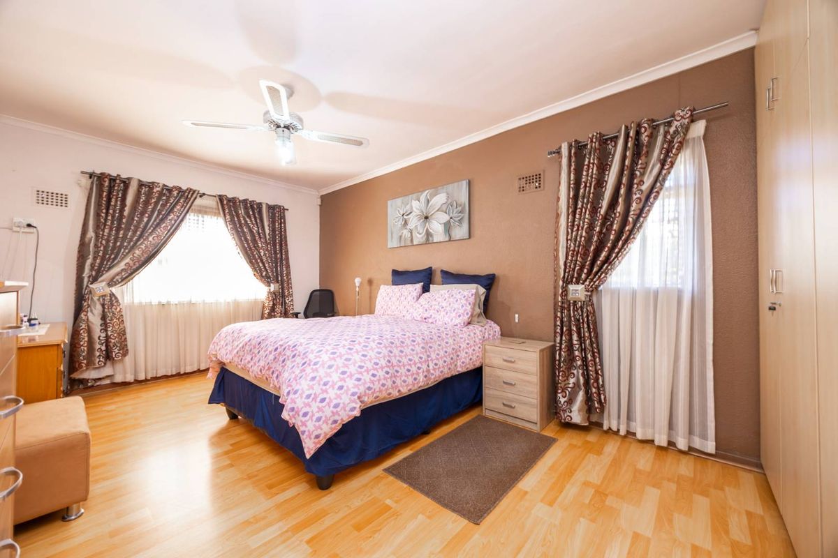 Spacious bedroom featuring laminate flooring, built-in cupboards, and a ceiling fan, offering a comfortable and functional living space.