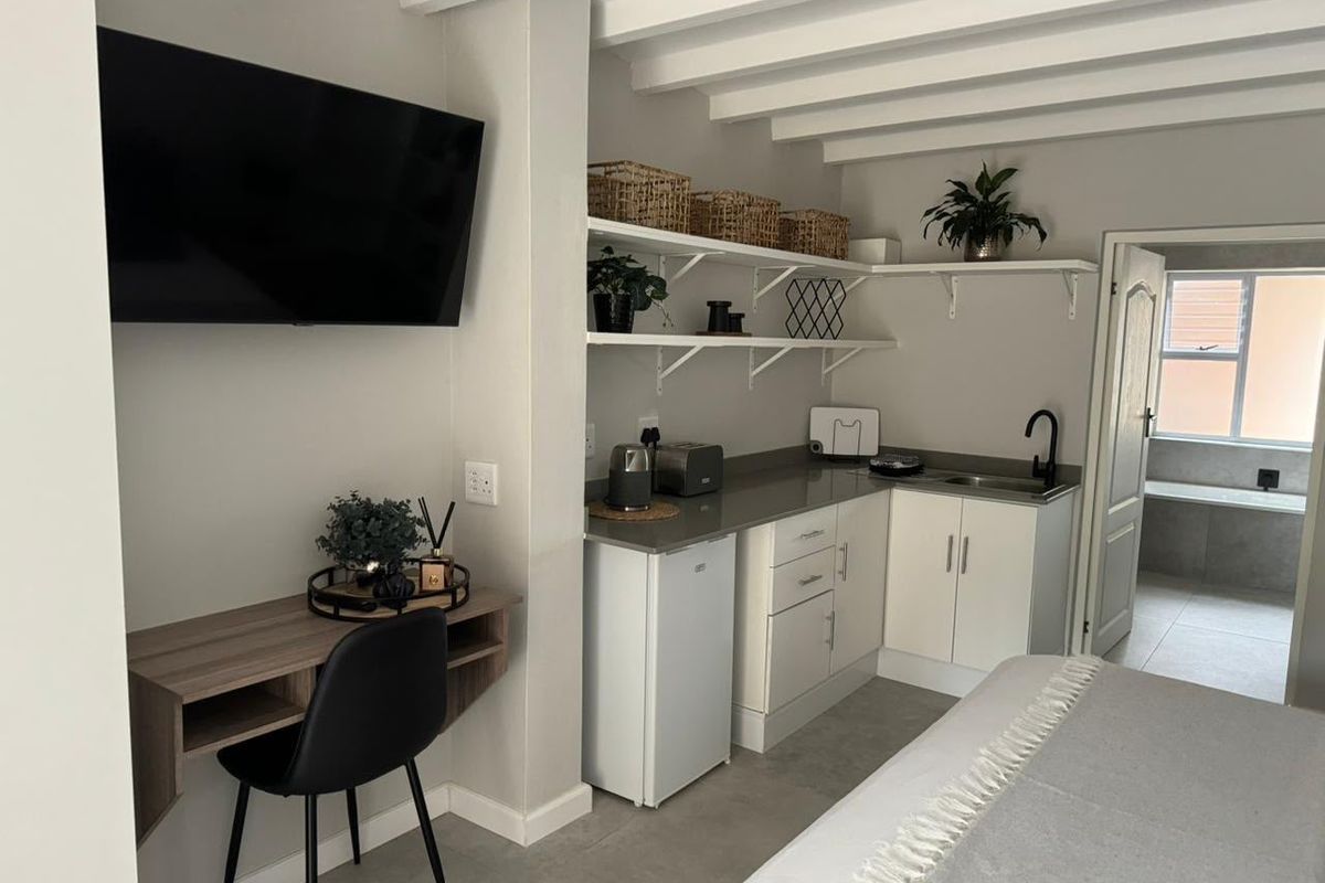 A compact kitchenette featuring white cabinetry, stone countertops, open shelving, and exposed ceiling beams, seamlessly integrated into a modern living space.