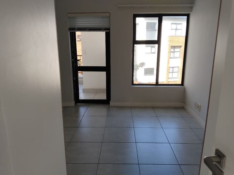 An empty, well-lit living area featuring neutral tiled flooring, large windows, and direct access to an outdoor balcony space.