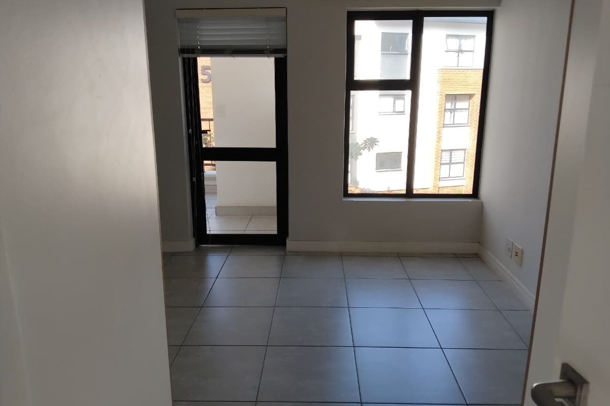 An empty, well-lit living area featuring neutral tiled flooring, large windows, and direct access to an outdoor balcony space.