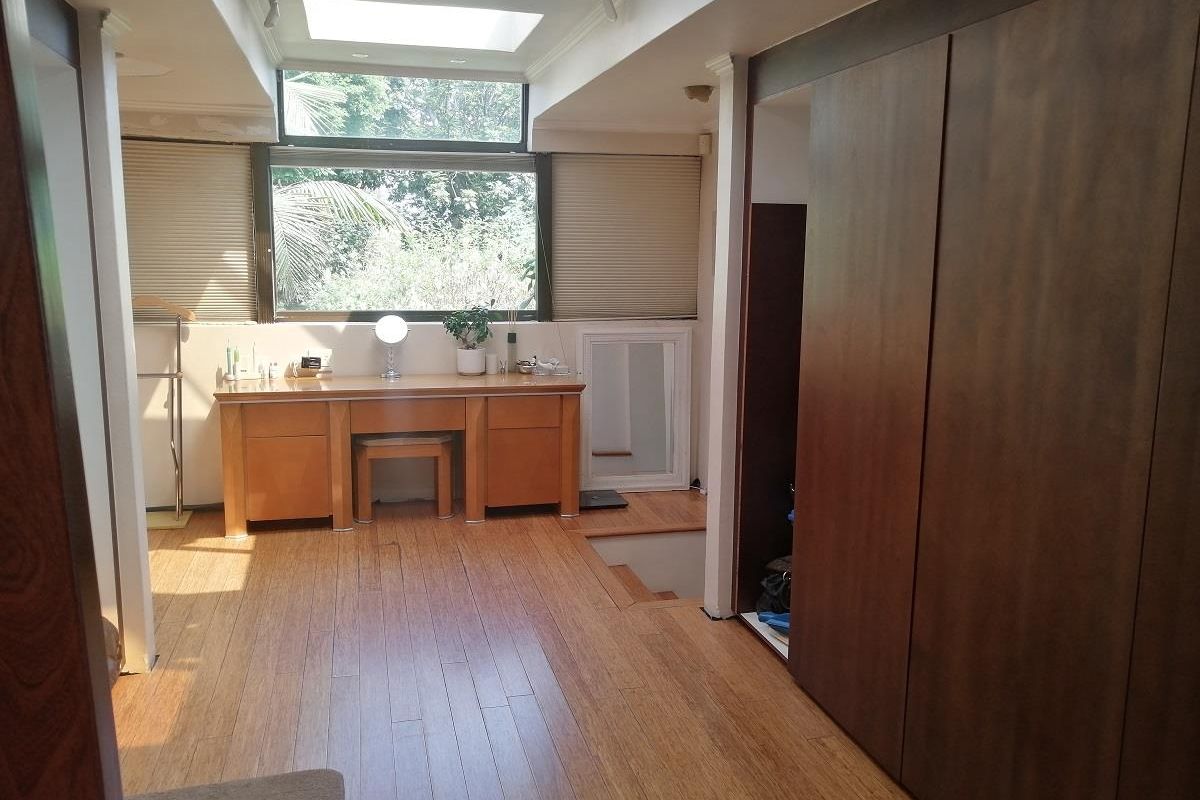 A bright bedroom featuring warm timber flooring, built-in wooden cabinetry, and a large skylight that provides ample natural light.
